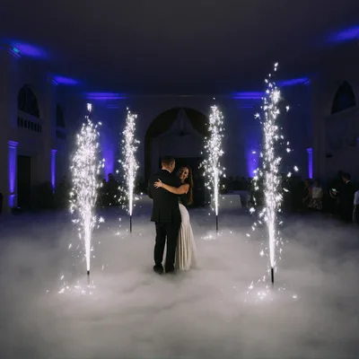 A couple's first dance framed by cold spark fountains, low fog across the floor and blue uplighting on the walls
