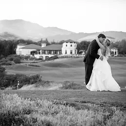 A couple kissing on the course at the Bridges Golf Club, the clubhouse and the San Ramon hills behind them