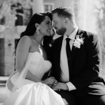 Melika and Cole seated together at their wedding, in black and white, Melika in a strapless gown and Cole with a boutonnière