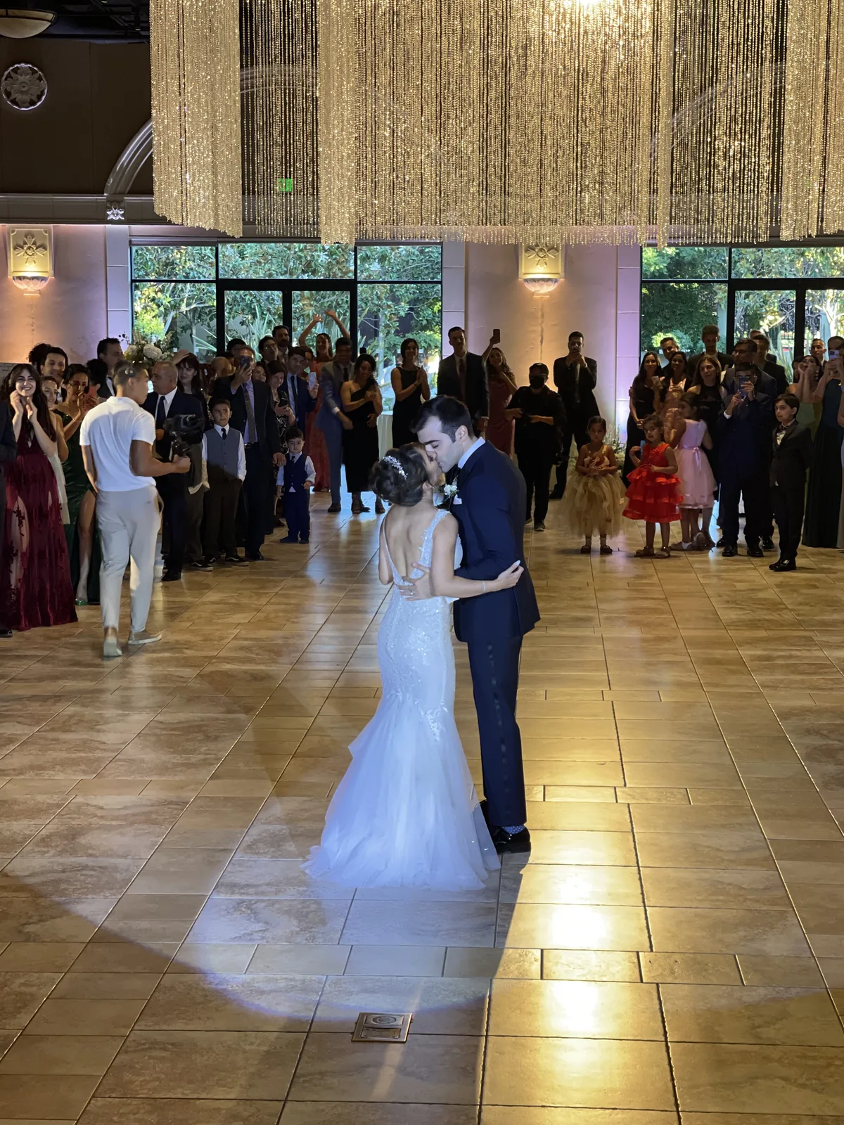 Mahsa and Arash's first dance under a crystal chandelier, a spotlight on the couple and guests filming from the edge of the floor