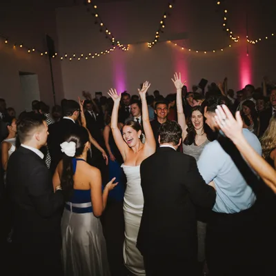 A full wedding dance floor at night, the bride laughing with her arms up in the middle of the guests